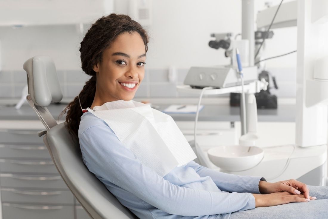 A patient smiling in a dental chair with a bib on, in a bright Cape Coral dentist office.