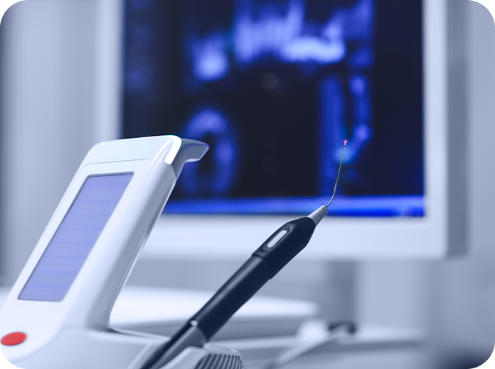 A dental tool with a red light is positioned in front of a monitor displaying dental images in a treatment setting.