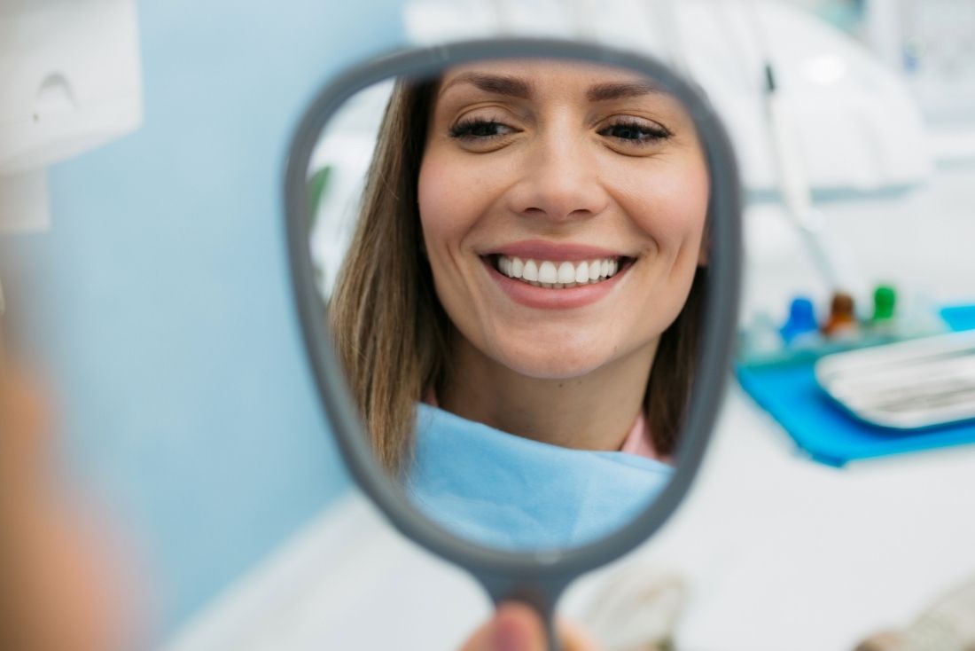 A patient smiles while looking into a dental mirror in a treatment room at a Cape Coral Dentist office.