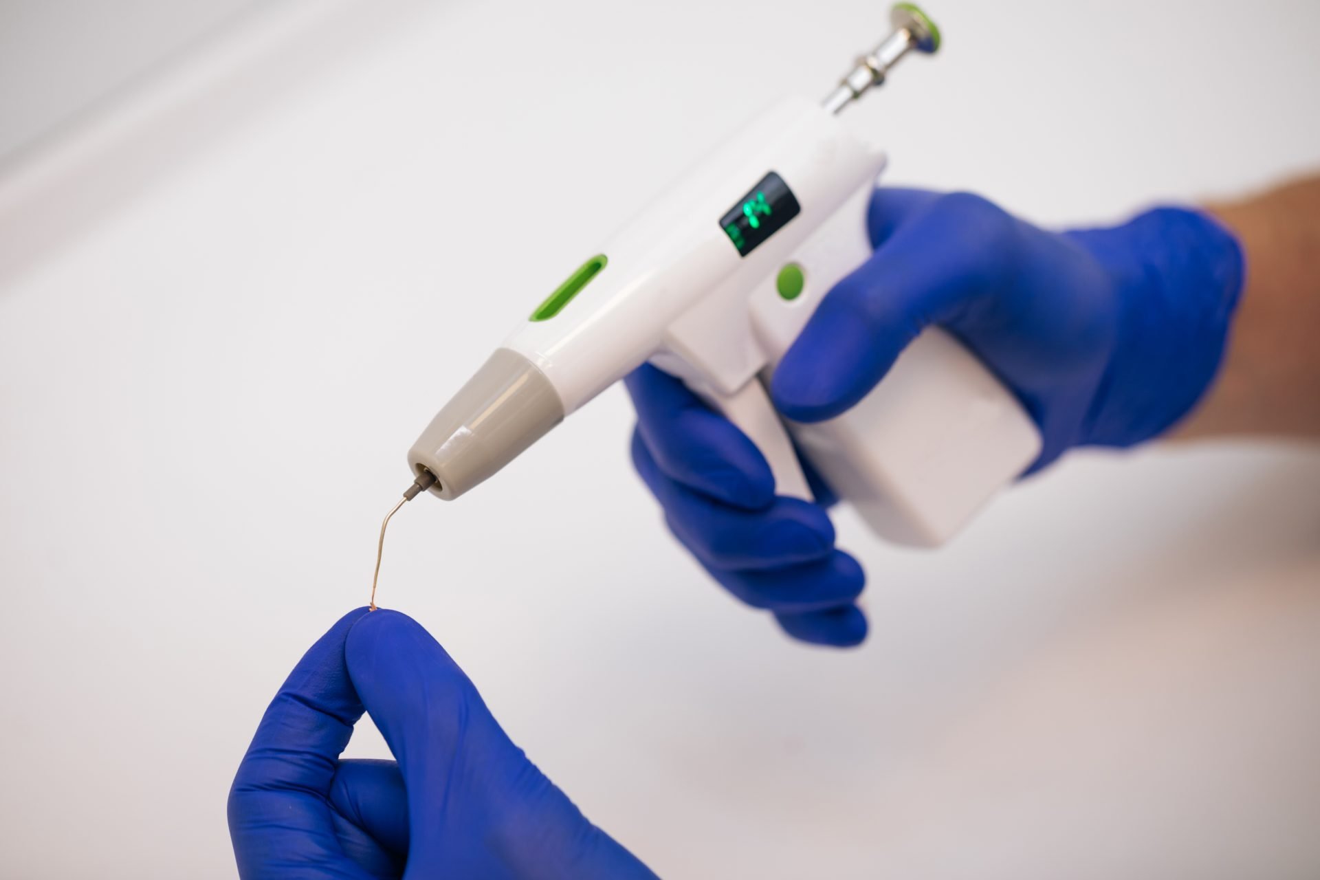 A dentist holding a dental device with a needle attachment while wearing blue gloves.