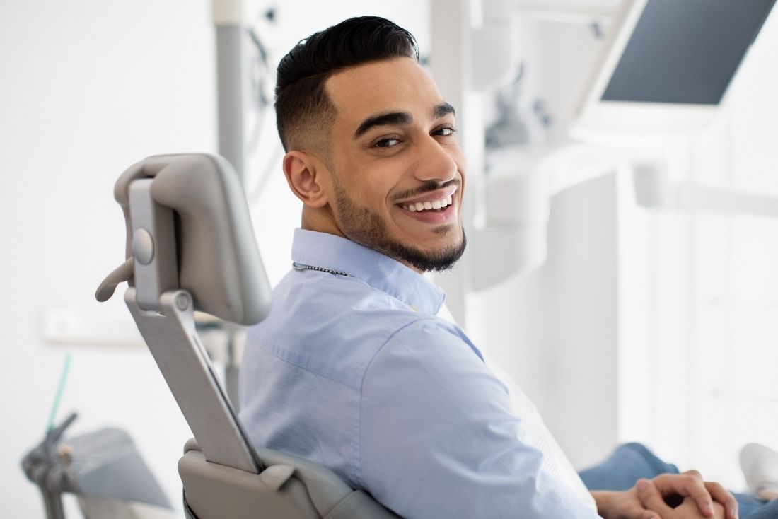 A smiling patient sitting in a dental chair in a bright dental office.