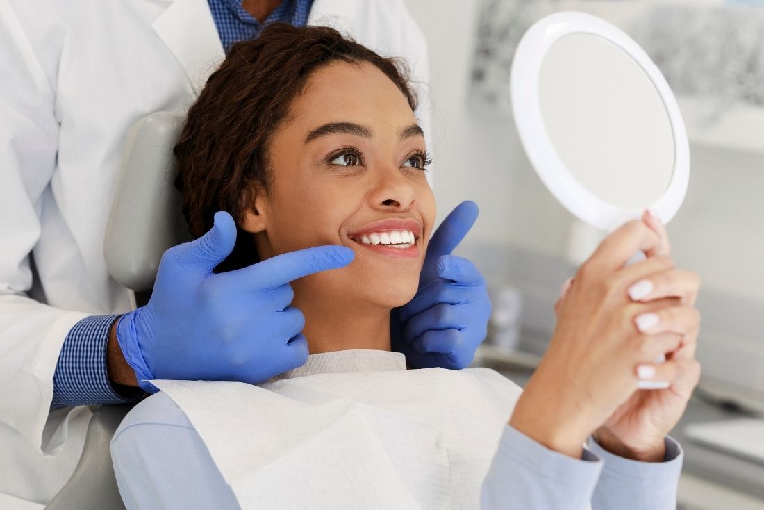 A dentist in Cape Coral is showing a patient her teeth in a mirror while pointing at her smile.