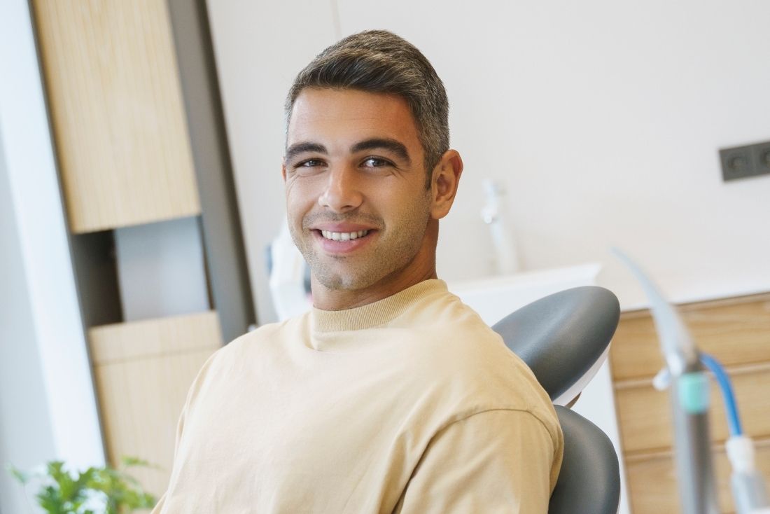 A smiling man sitting in a dental chair in a bright, modern dental office.